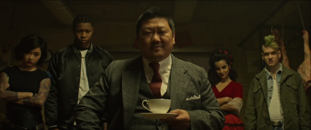 Benedict Wong as the refined Master Lin with Saya, Willie, Maria and Billy (Liam James) in the background. Master Lin sits calmly with his tea cup and saucer. (SyFy/Screencap)