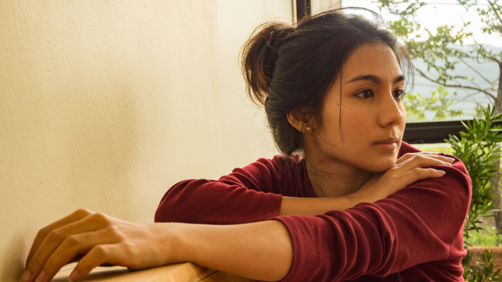 An Asian woman in a red sweater looks away.