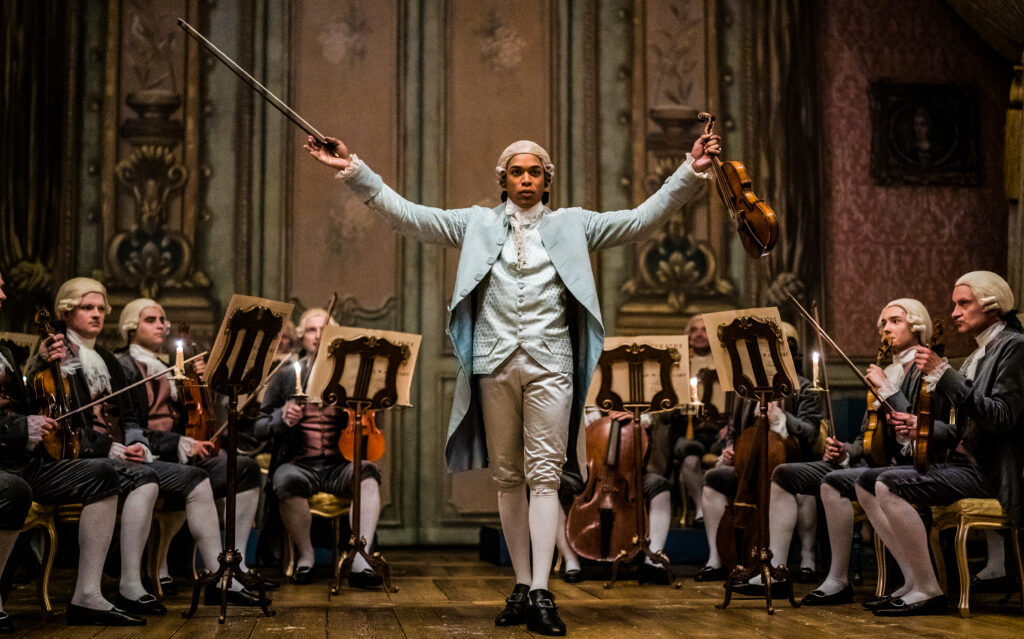 Kelvin Harrison Jr. in the film CHEVALIER, in a confident pose as he is accompanied by a string chamber orchestra. Photo by Larry Horricks. Courtesy of Searchlight Pictures. © 2022 20th Century Studios All Rights Reserved.