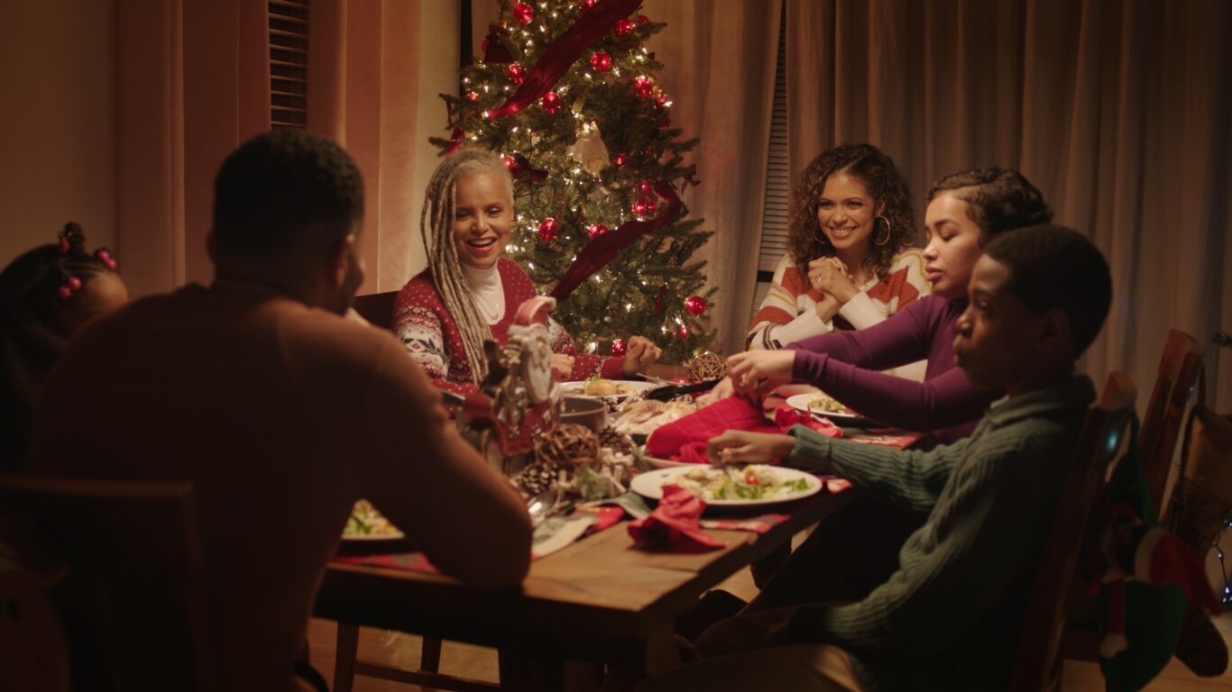 The cast of Blended Christmas sit around a Christmas table.