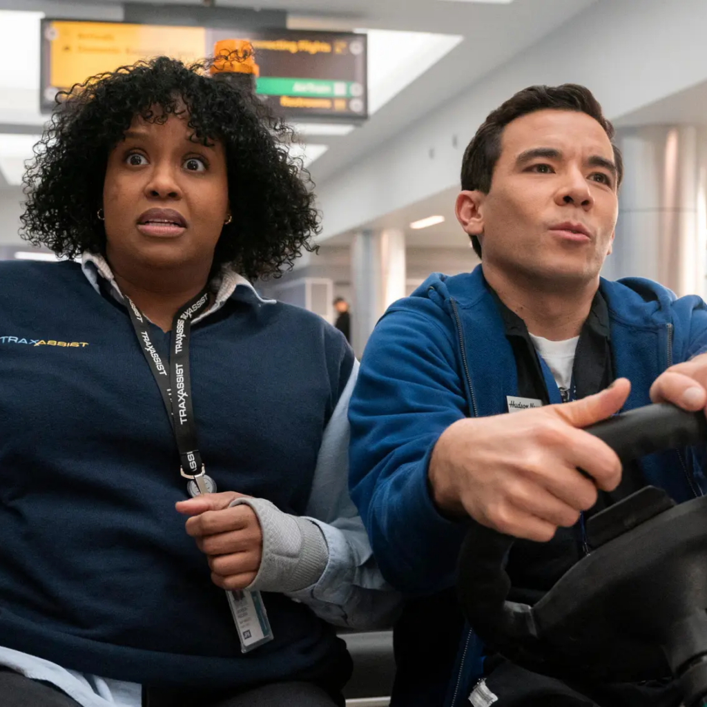 Natasha Rothwell and Conrad Ricamora are speeding in an airport transport vehicle. 