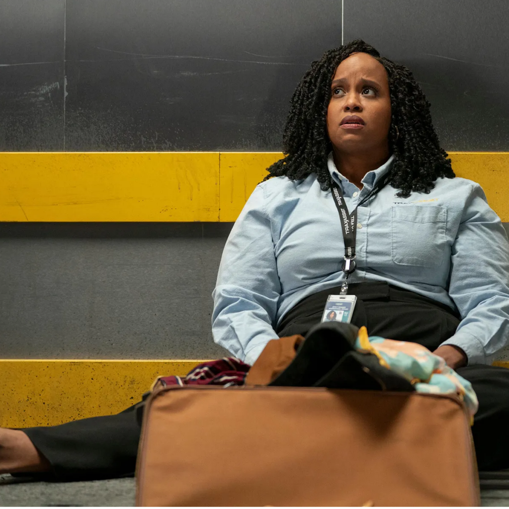 Natasha Rothwell sits on the floor of an elevator, looking concerned. 